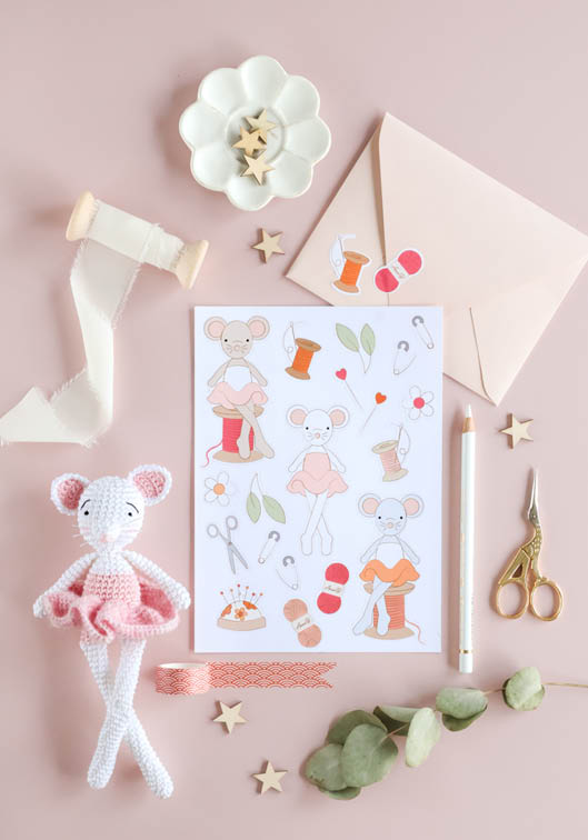 Mise en scène créative avec souris amigurumi crochetée, illustrations kawaii couture et accessoires de mercerie sur fond rose pastel, idéale pour crochet DIY, loisirs créatifs, papeterie artisanale et univers handmade enfantin